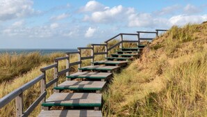 A wooden staircase leading to a beach with a railing on one side and grass on the other.