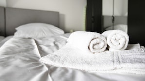 A neatly made bed with white linens and rolled towels.
