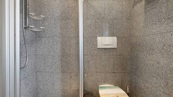 Eine Dusche mit Glastür, eine Toilette mit Papierhandtuchspender und ein Mülleimer.
