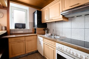 Una cucina compatta con mobili in legno, un forno a microonde, una lavastoviglie, un piano cottura e una finestra.