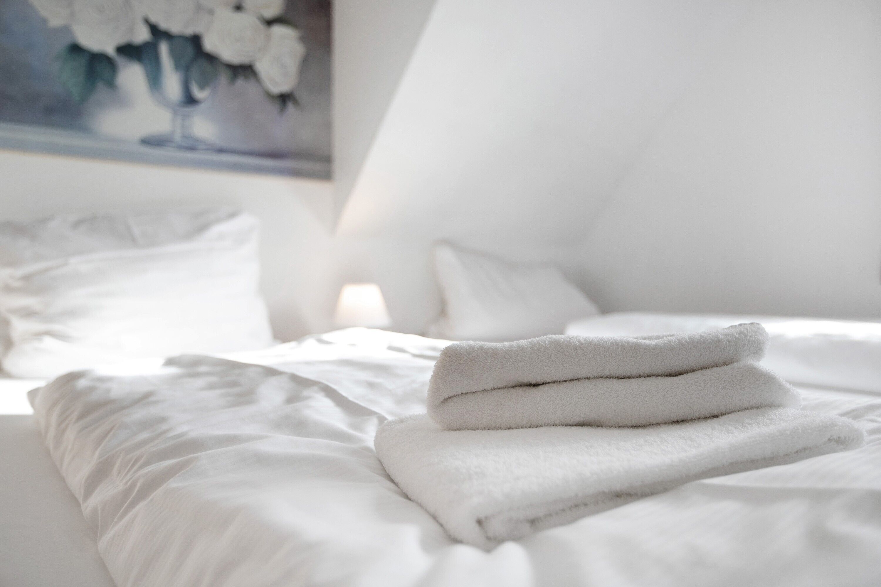 A neatly made bed with white linens and a folded towel on top.