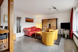 Una sala de estar con un sofá rojo, un sillón amarillo, un aparador de madera y un televisor.