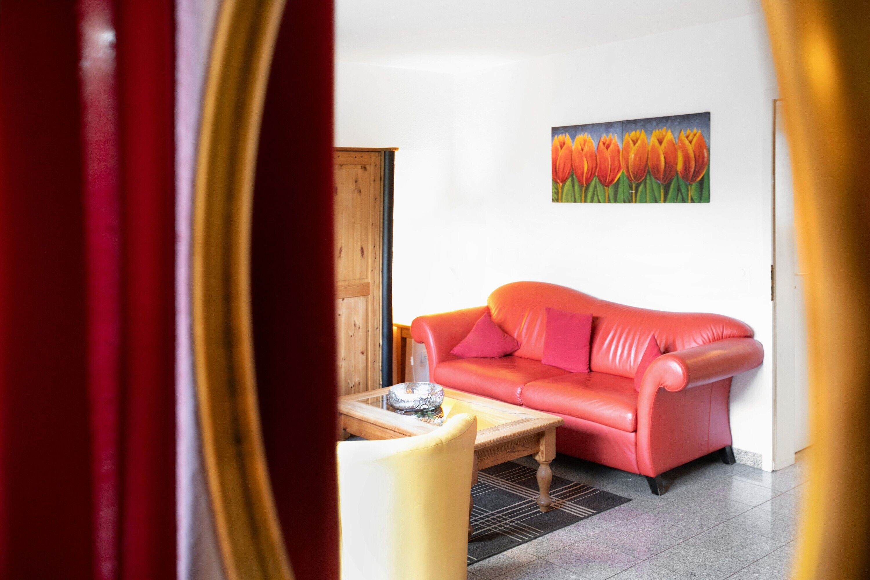 A room with a red sofa, a wooden coffee table, and a painting of tulips on the wall.