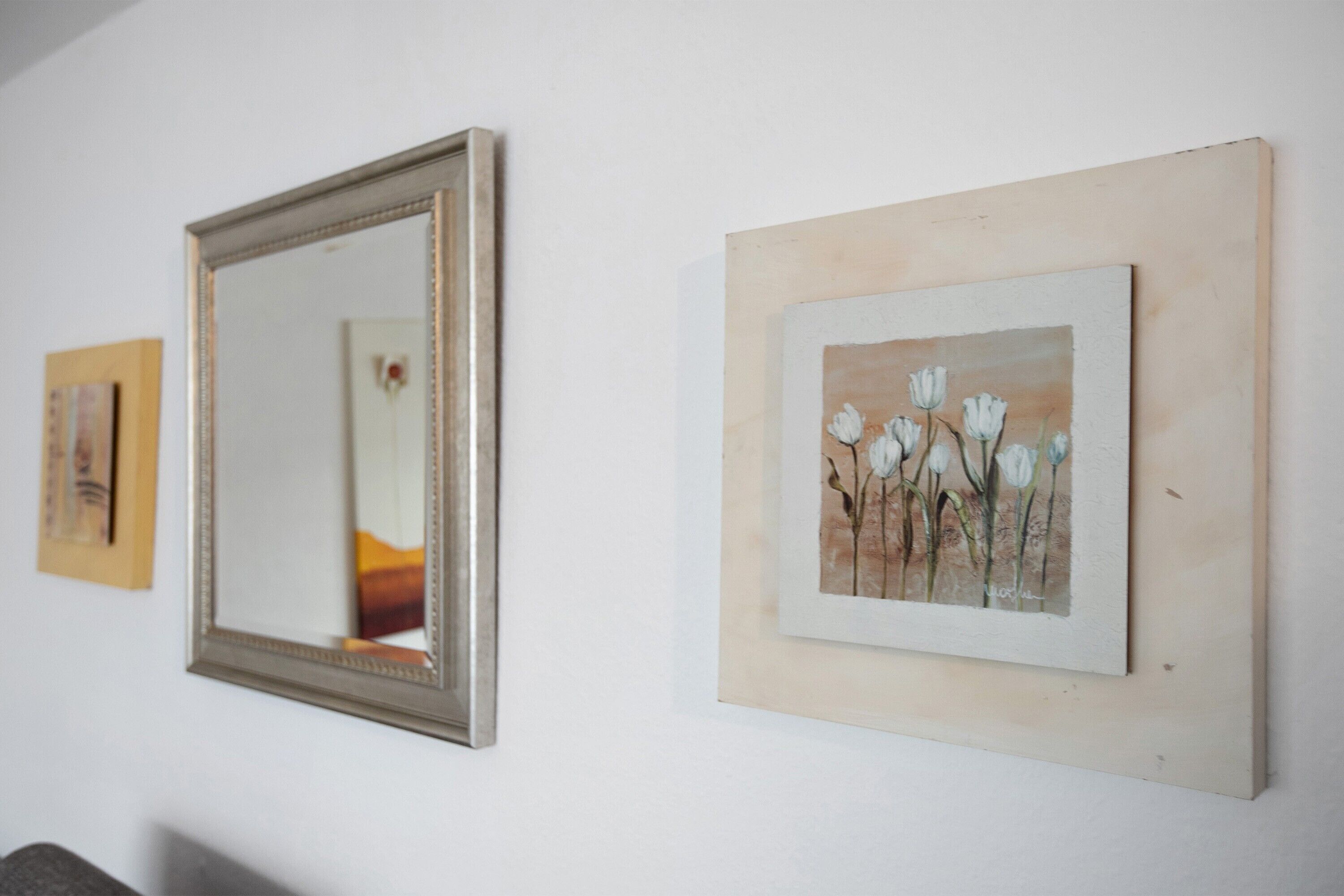 Una pared con tres obras de arte enmarcadas, incluyendo un espejo y dos cuadros.