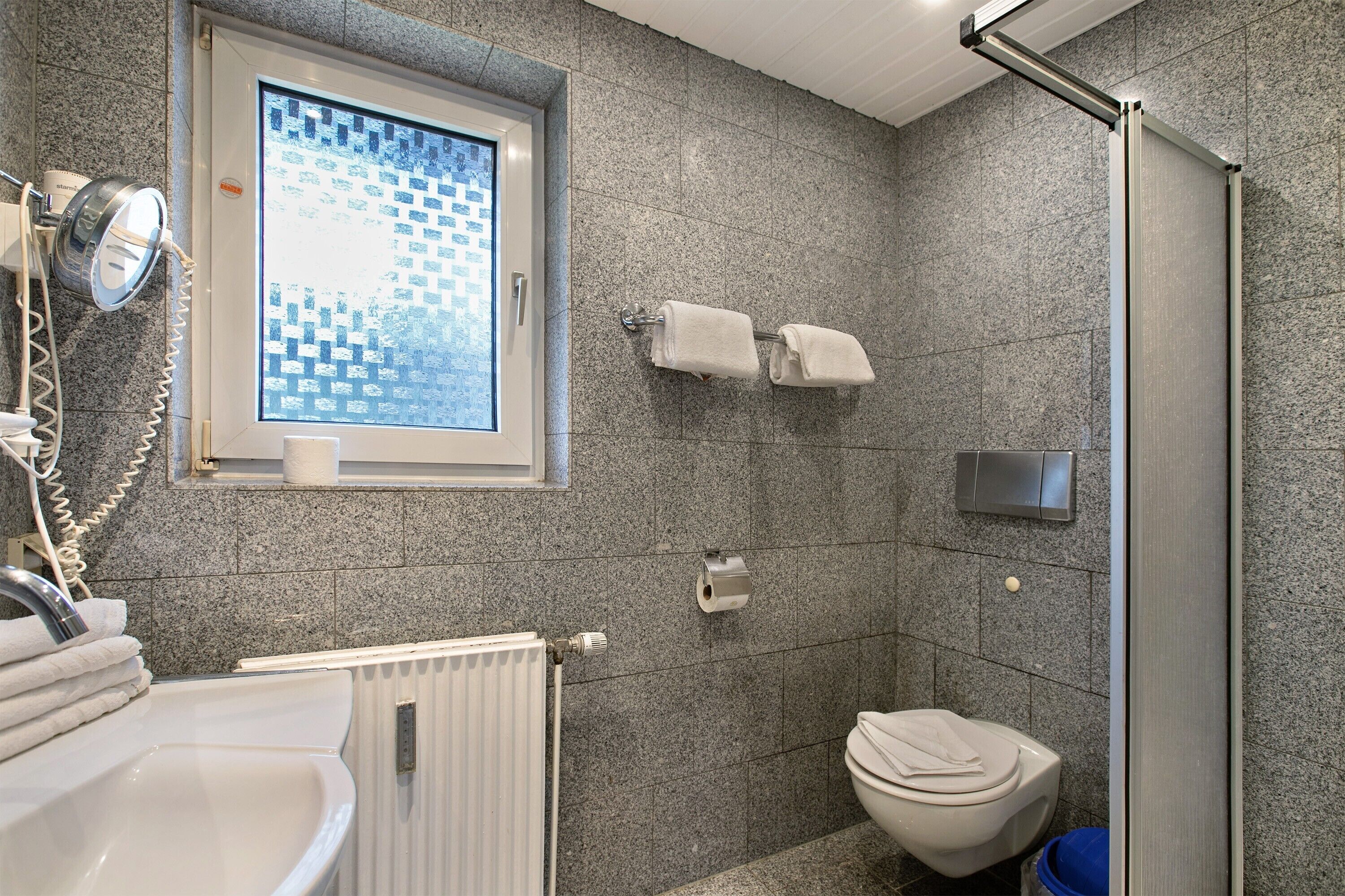 A bathroom with a shower, toilet, sink, and a window with a view.