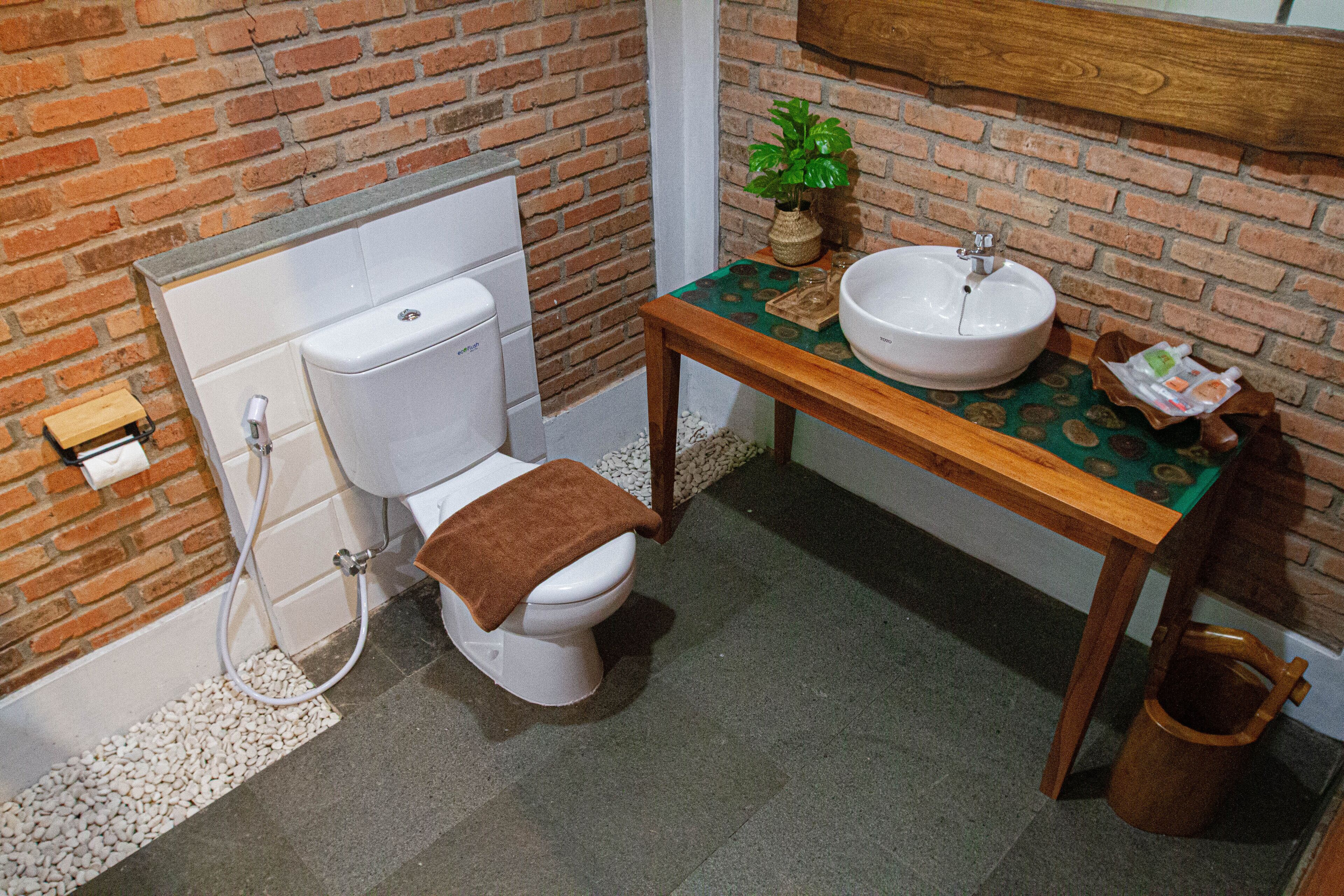 Un baño con inodoro, lavabo y una mesa de madera con mantel estampado verde.