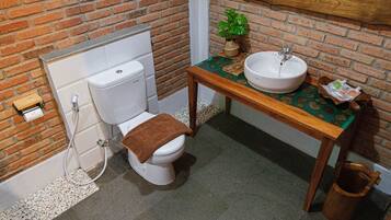 Un baño con inodoro, lavabo y una mesa de madera con mantel estampado verde.