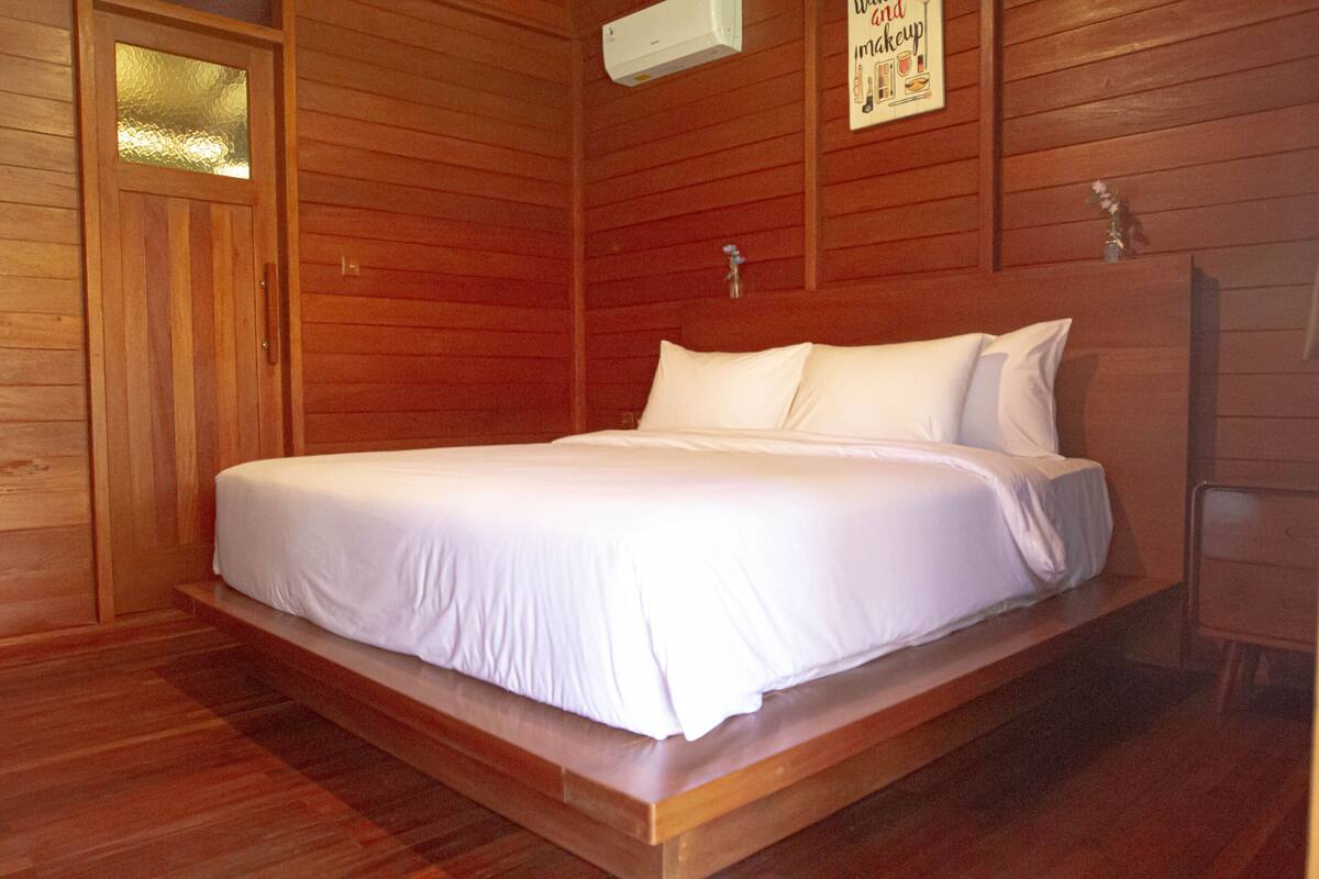 A wooden-paneled room with a bed, a door, and a wall-mounted air conditioner.