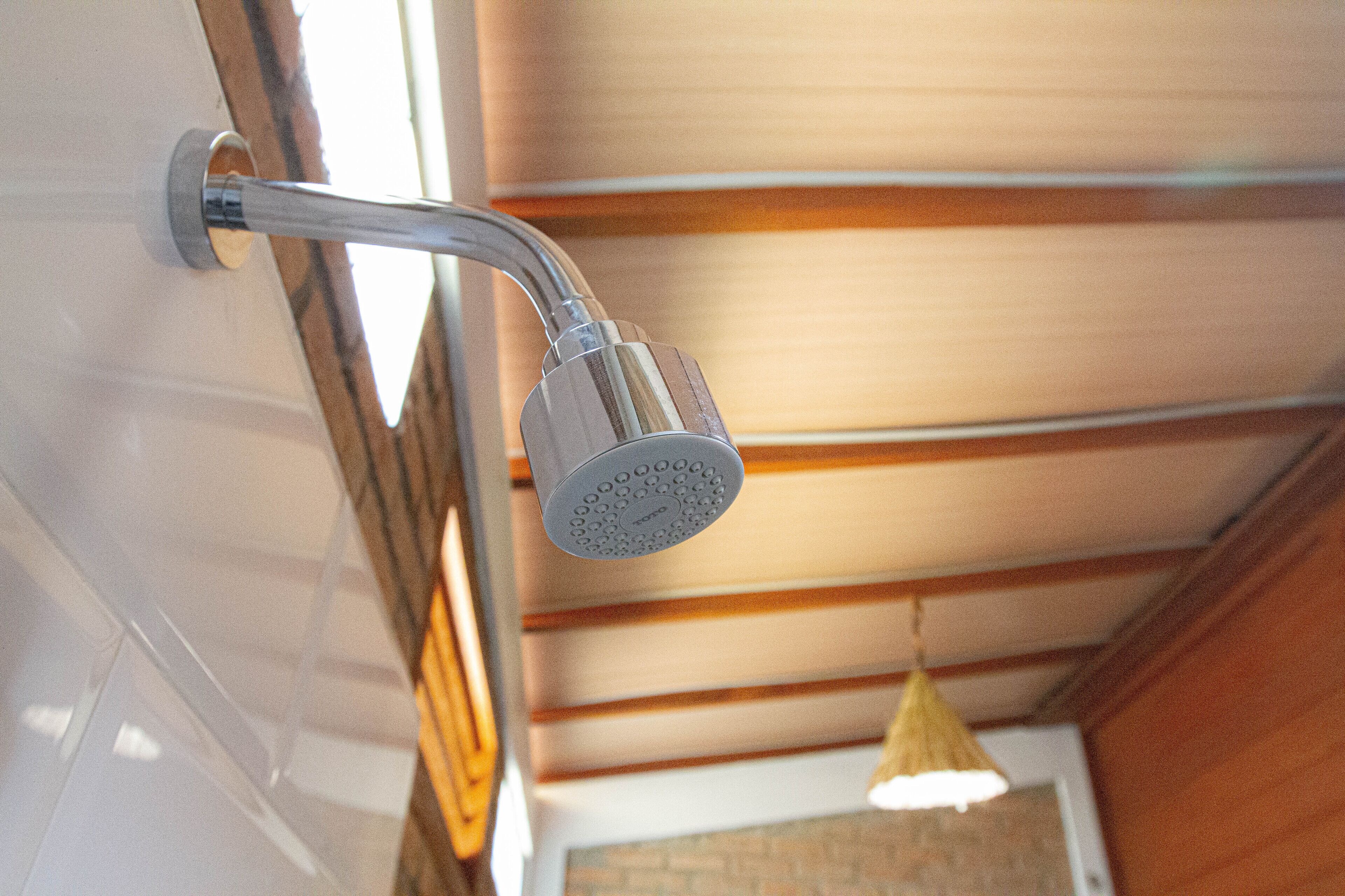 Ett duschmunstycke monterat på en vägg, med ett träpanelat tak och en hängande lampa.