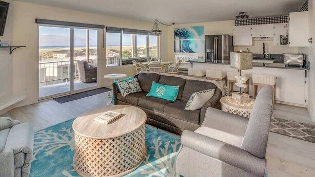 A spacious living area with a large window, a dining table, and a kitchen area. - Pacific View V484 (Gearhart)