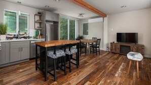 A modern kitchen with wooden flooring, a central island, and a dining area with chairs.