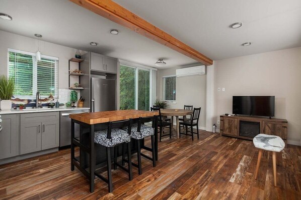 A modern kitchen with wooden flooring, a central island, and a dining area with chairs.