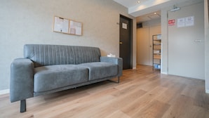 A modern living room with a grey sofa, wooden flooring, and a door with a sign. - JA Hotel Namba (Osaka)