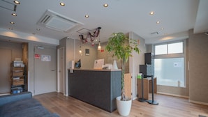 A reception area with a wooden floor, a reception desk, a potted plant, a seating area, and a window with a view. - JA Hotel Namba (Osaka)