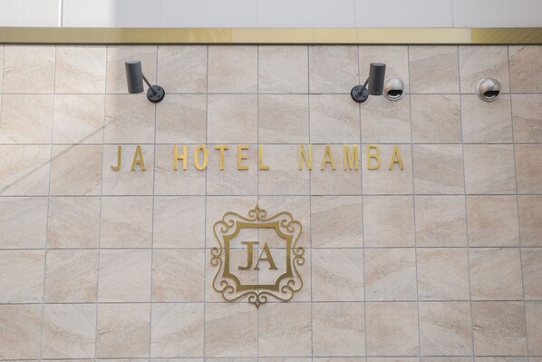 A tiled wall with the text "JA HOTEL NAMB" and a decorative "JA" emblem.