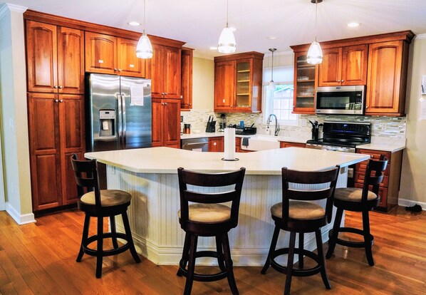 A kitchen with wooden cabinets, stainless steel appliances, and a central island with bar stools. - Rustic Lakehouse Oasis - Hot Tub, Game Room, Fire Pit, and Fishing Rods (Roxboro)