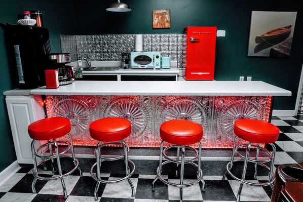 A kitchen with a bar area featuring four red stools, a red refrigerator, and a microwave. - Rustic Lakehouse Oasis - Hot Tub, Game Room, Fire Pit, and Fishing Rods (Roxboro)