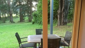 Eine überdachte Terrasse mit Tisch und Stühlen, eine Holzterrasse und Blick auf eine Rasenfläche mit Bäumen.