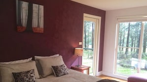 Ein Schlafzimmer mit einem großen Bett, einem Nachttisch, einer Lampe und einem Fenster mit Blick auf Bäume.