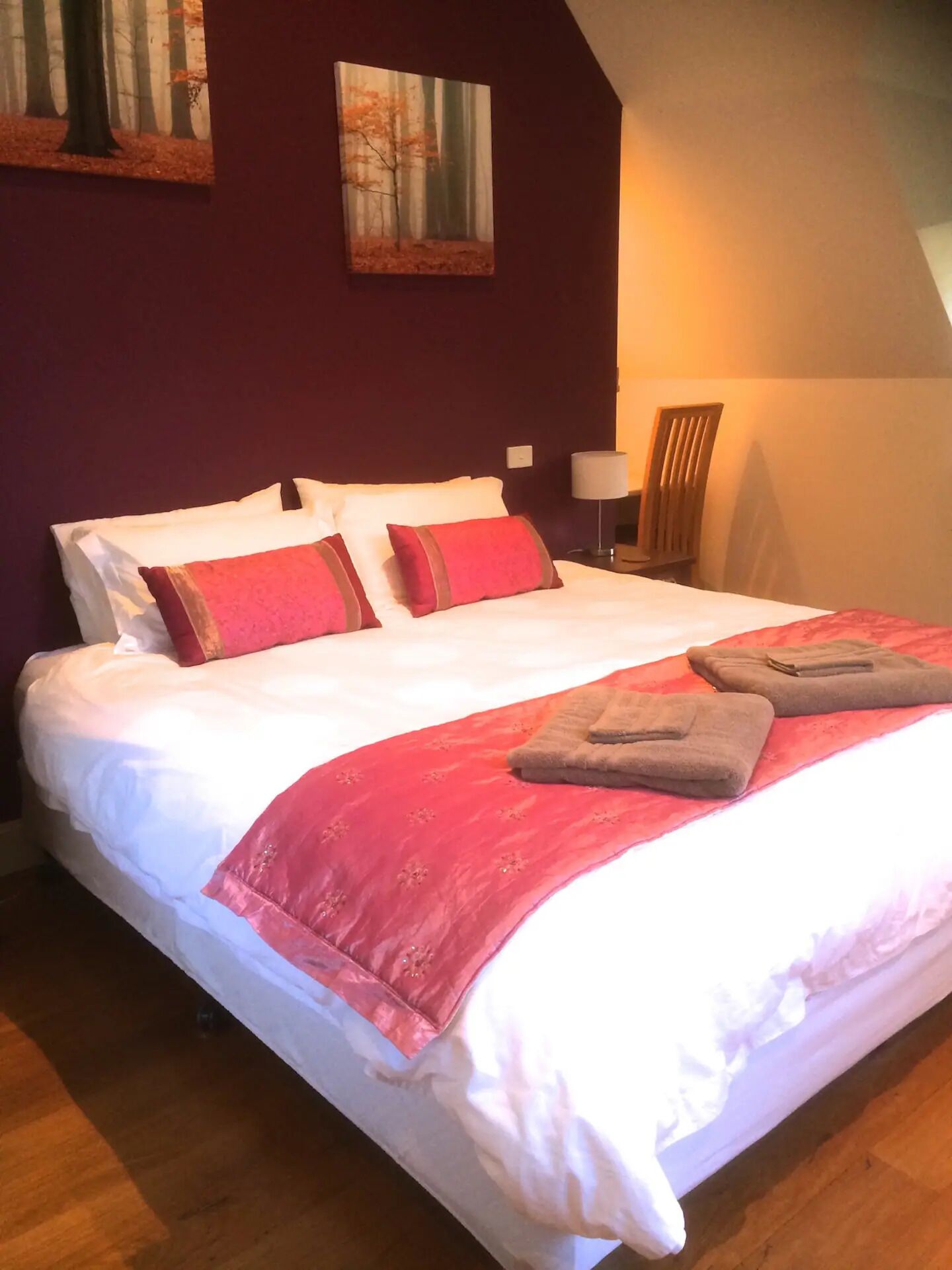 Un letto rifatto con biancheria bianca e rossa, una coperta rossa e due asciugamani piegati.