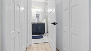 A hallway leading to a bathroom with white doors, a marble countertop, and a shower area.