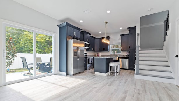 A modern kitchen with dark cabinets, a stainless steel refrigerator, and a large island.