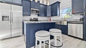 A modern kitchen with dark blue cabinets, stainless steel appliances, a granite countertop, and two white stools.