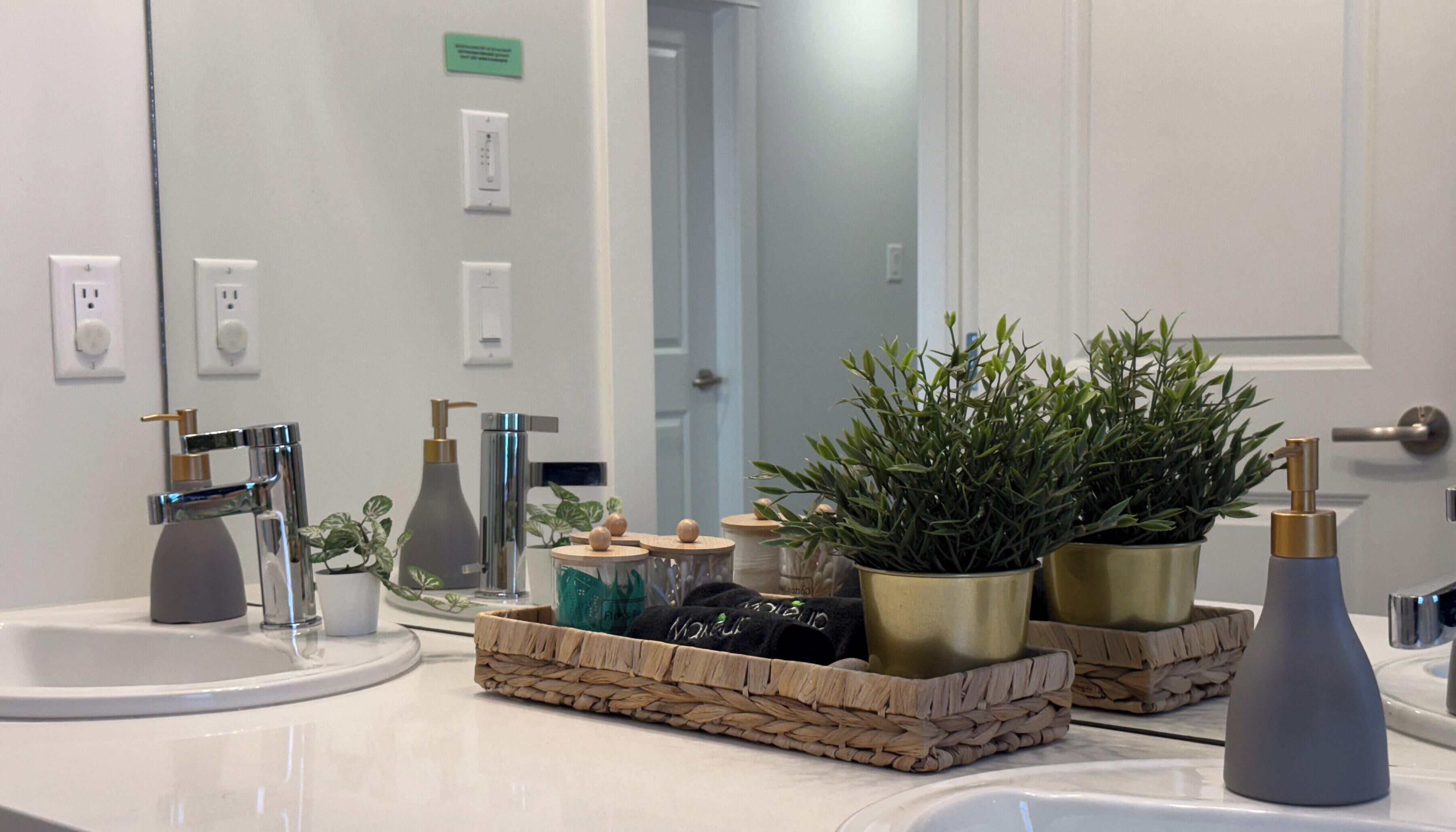 A bathroom with two sinks, a mirror, and a door. There are plants and decorative items on the counter.