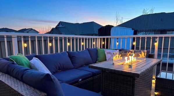 Un balcon avec un canapé, une table dotée d’un foyer et des guirlandes lumineuses.
