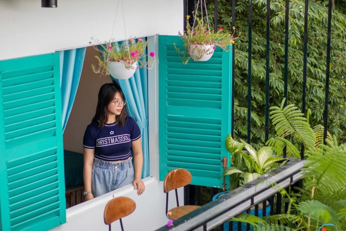 A balcony with turquoise shutters, a hanging plant, and a person standing.