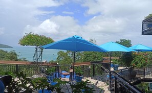 A seaside patio with blue umbrellas, outdoor seating, and a view of the ocean. - The Nam Du Hill (Kien Hai)