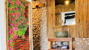 A rustic bathroom with a stone wall, wooden vanity, and a decorative floral panel.
