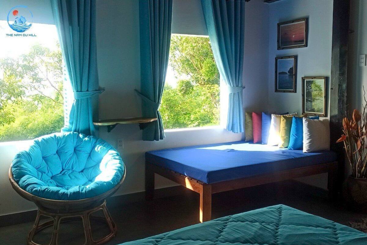 A room with a bed, a blue chair, and a window with curtains.