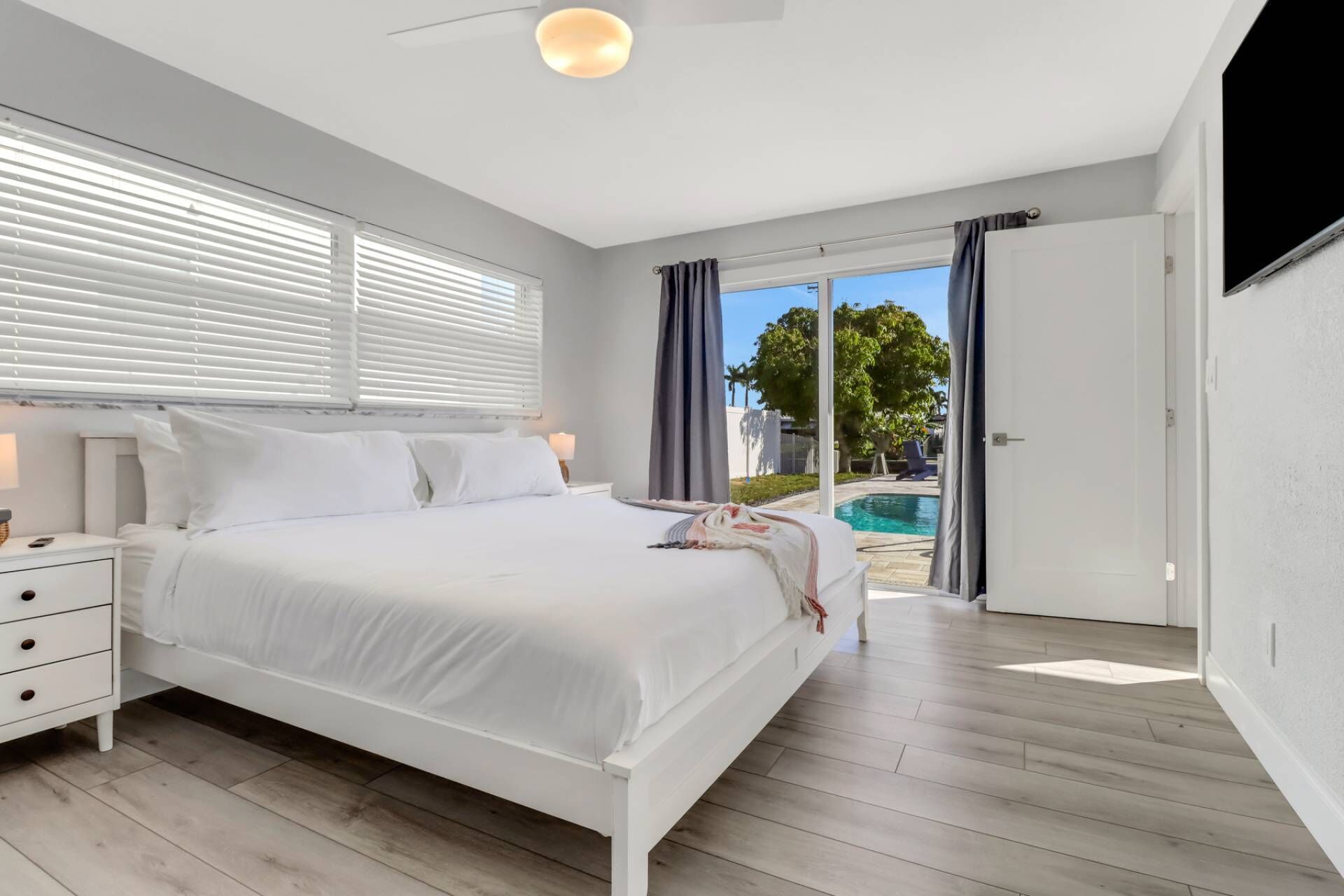 A modern bedroom with a large bed, a bedside table, and a view of a swimming pool.