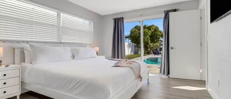 A modern bedroom with a large bed, a bedside table, and a view of a swimming pool.