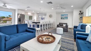 Una sala moderna con un sofá azul, una mesa de centro blanca y una zona de comedor con sillas blancas.