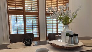 A dining area with a table set for two, featuring a vase of white flowers, a coffee mug, and a tea set.
