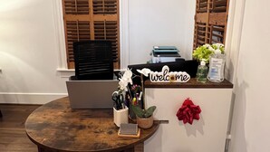 A reception desk with a laptop, a 'welcome' sign, a vase with flowers, and a red bow.