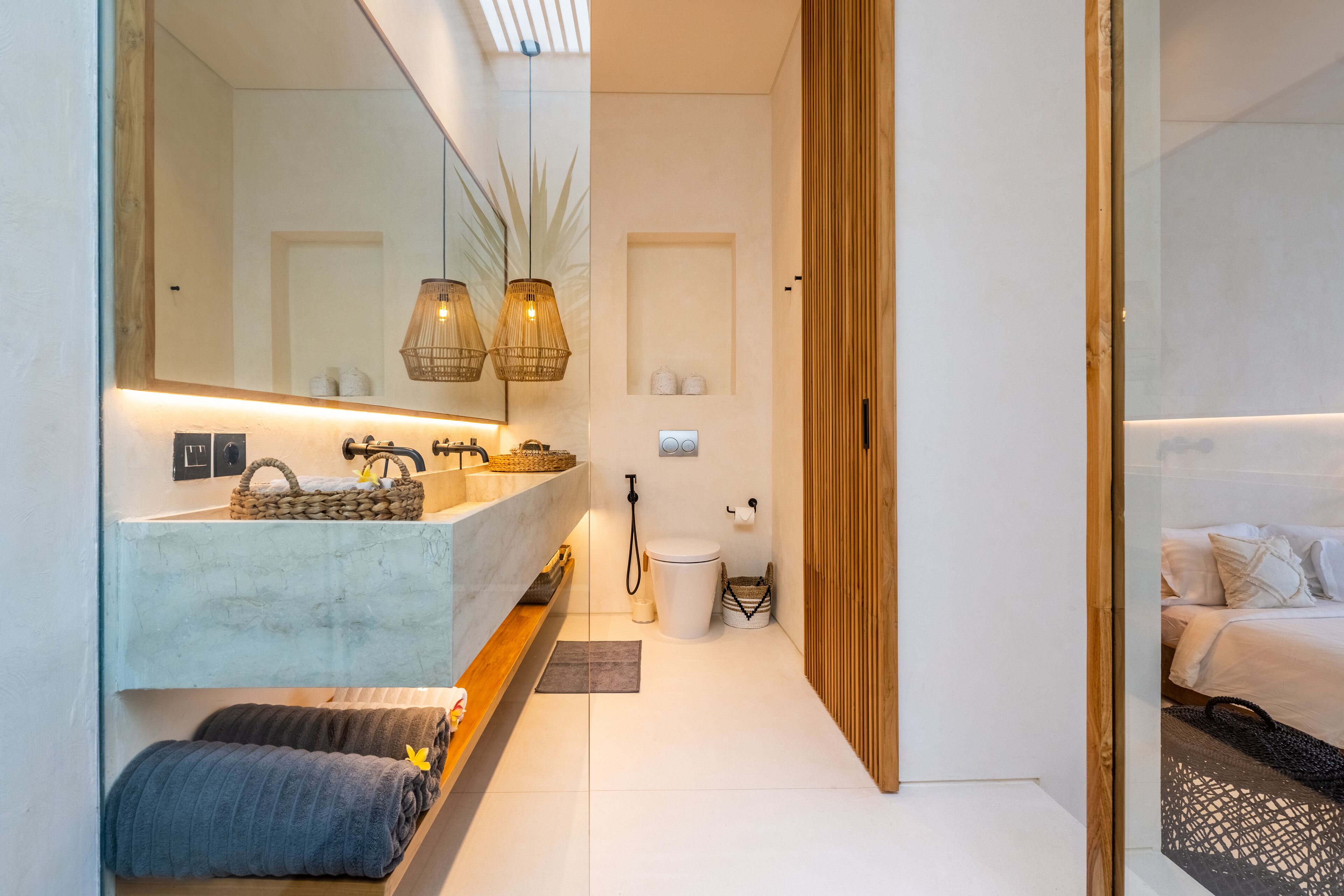 A modern bathroom with a large mirror, a sink with a marble countertop, a toilet, and a shower area.