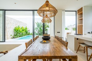 Un comedor con una mesa de madera, sillas de mimbre y un colgador de luces.