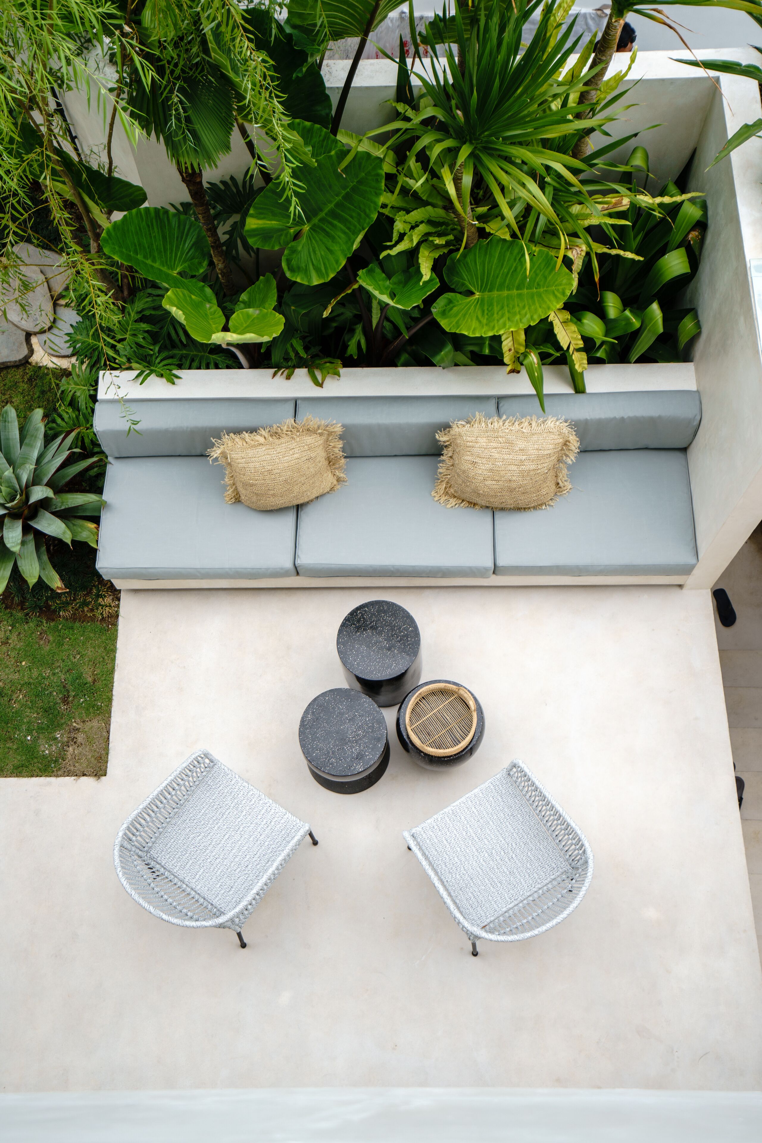 A modern outdoor seating area with a gray sofa, two woven cushions, and two white woven chairs.