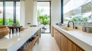 A modern kitchen with a large island, wooden cabinets, and a view of greenery outside. - Casa Umalas Villa by Betterplace (Kerobokan)
