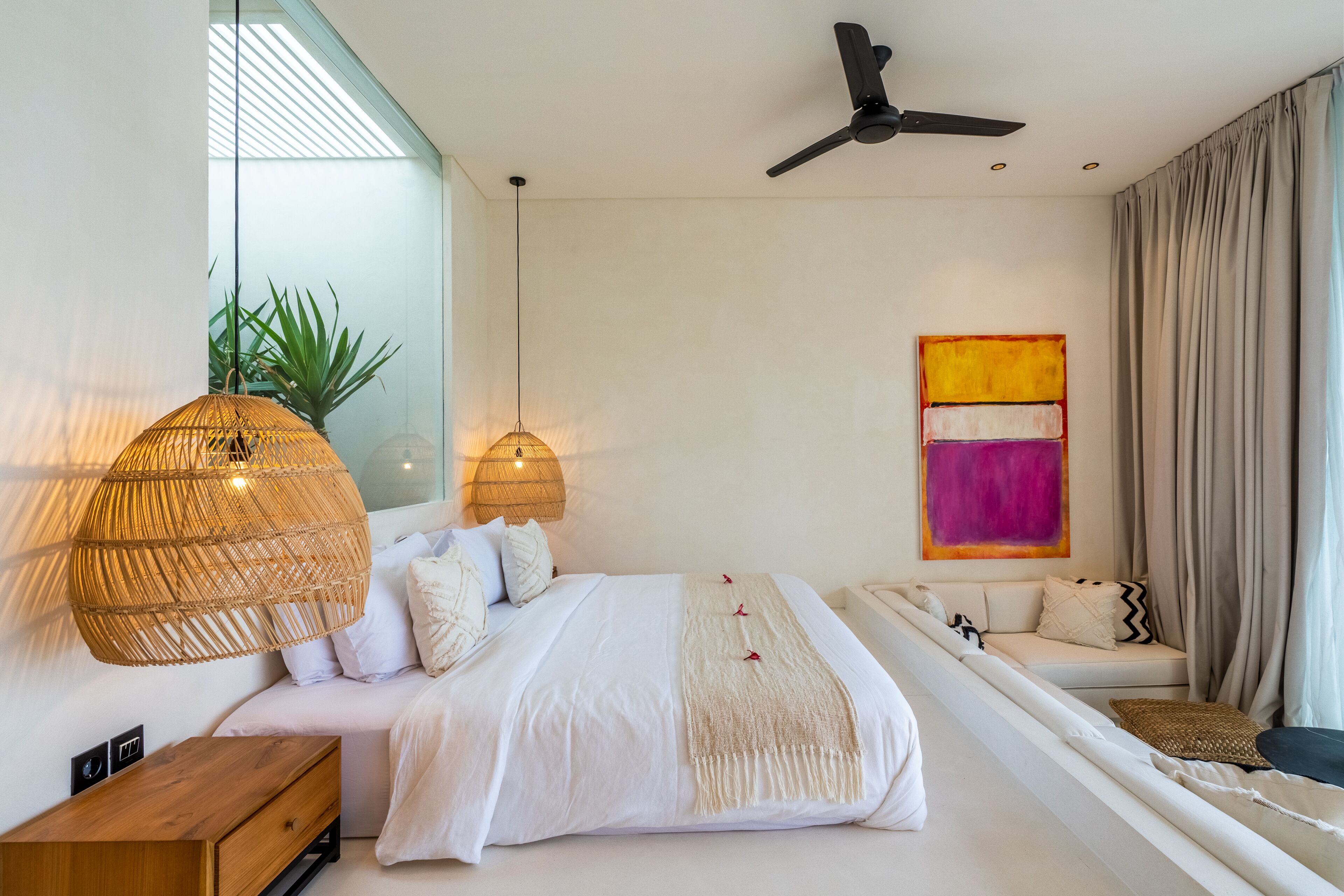 Ein modernes Schlafzimmer mit Bett, Nachttisch, hängender Rattan-Lampe und Deckenventilator.