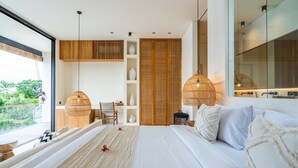 A modern bedroom with a large bed, a sitting area with a chair, and a view of greenery outside. - Casa Umalas Villa by Betterplace (Kerobokan)
