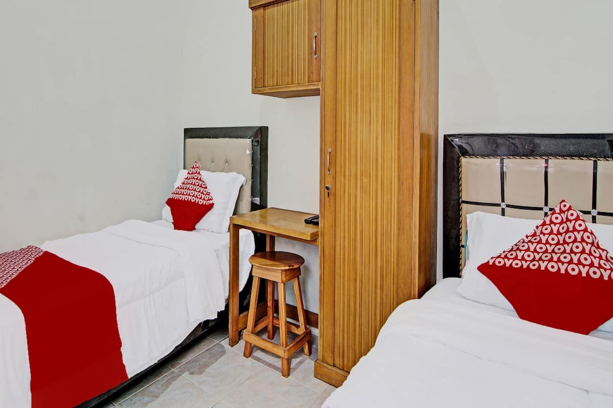 A room with two beds, each with a red and white patterned pillow, a wooden stool, and a small table.