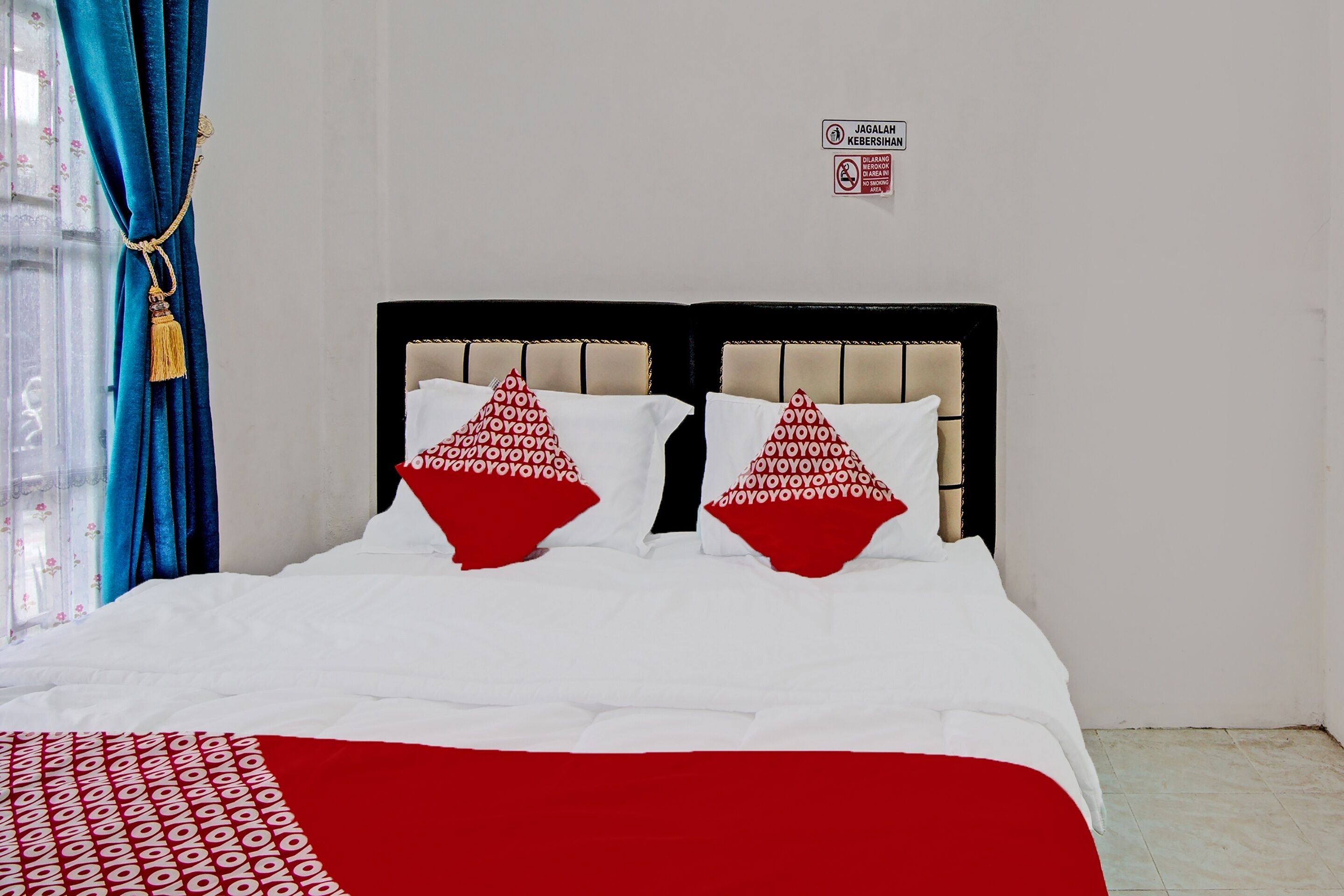 Ein Bett mit weißroter Bettdecke, zwei Kissen mit rotweißer Musterung und ein Schild an der Wand.
