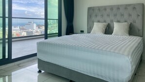 A modern bedroom with a large bed, a grey tufted headboard, and two patterned pillows. - Arcadia Millennium Tower by PSR (Pattaya)