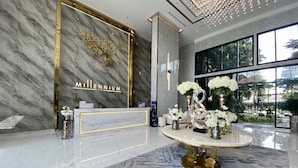A reception area with a marble wall, a gold and white sign, and a round table with white flowers. - Arcadia Millennium Tower by PSR (Pattaya)