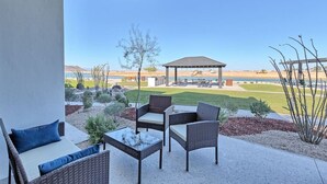 Un patio al aire libre con mobiliario de mimbre y vistas a un campo deportivo y un pabellón.