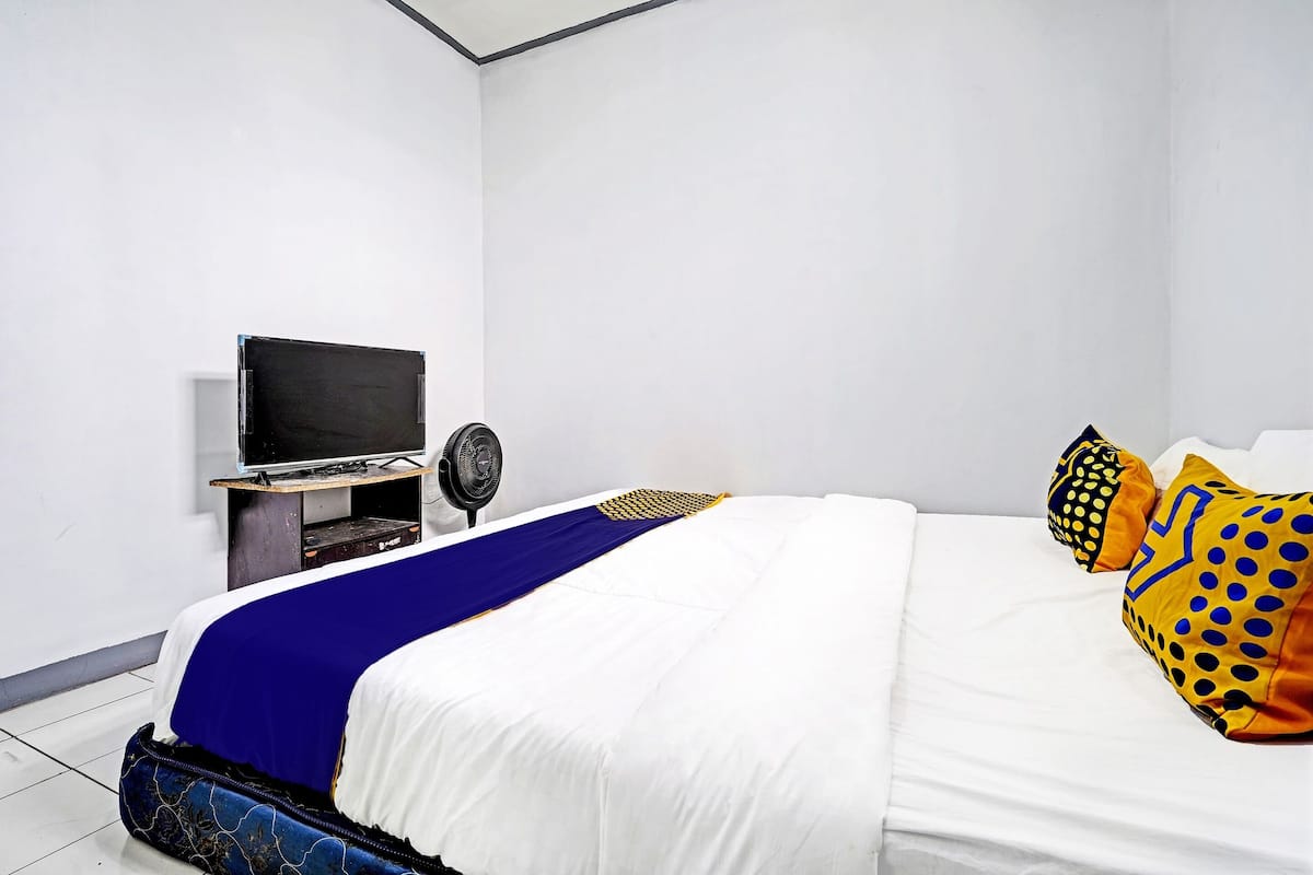 A bedroom with a bed, a TV, a fan, and a suitcase.